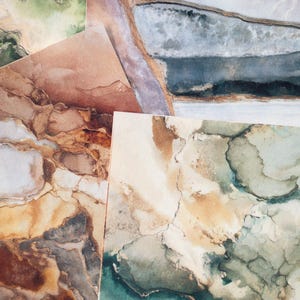 May include: A collection of abstract art prints featuring watercolor designs. The prints showcase a variety of earth-toned colors, including shades of brown, green, and blue, with intricate patterns resembling natural formations.