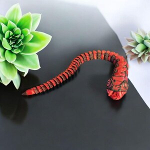 May include: A red and black segmented snake figurine with a detailed head and a textured surface.