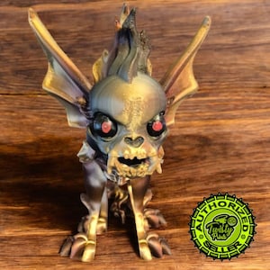 May include: A 3D printed figurine of a small, skeletal creature with large ears, a spiky head, and glowing red eyes. The figurine is painted in shades of gold, brown, and black. The figurine is standing on a wooden surface. The image also includes a circular sticker with the text "AUTHORIZED SELLER" and "Twisty Prints".