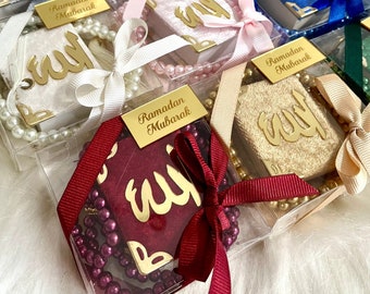 May include: Assortment of small gift boxes with gold calligraphy, each containing a set of prayer beads. The boxes are wrapped in various colors, including pink, purple, blue, green, and red. Each box has a tag that reads "Ramadan Mubarak".