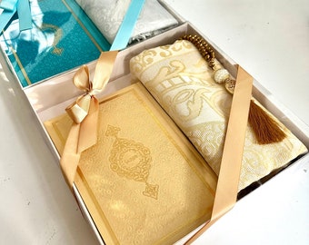May include: A gift set for prayer, featuring a blue prayer rug, a gold prayer rug, a gold-colored book, and a set of prayer beads with a tassel.