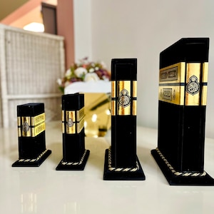 May include: Four black velvet bookends with gold trim and Arabic script. The bookends are arranged in order of size, with the largest on the right and the smallest on the left.