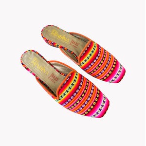 May include: A pair of colorful, patterned slip-on shoes. The shoes feature a vibrant design with vertical stripes in shades of pink, orange, yellow, and green. The interior is tan with the text "AINDINA FOODS".