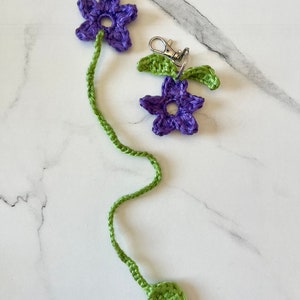 May include: A purple crocheted flower keychain with a green stem and leaves. The keychain has a silver metal ring.