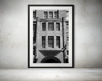 May include: Black and white photograph of a building with a large arched doorway and multiple windows. The building has a stone facade and is framed in a black frame.