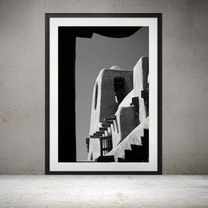 May include: Black and white photograph of a building with a unique architectural style. The building is made of adobe and has a series of steps leading up to the top. The photograph is framed in a black frame.