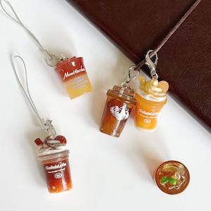 Puede incluir: Una colecci&oacute;n de dijes en miniatura con forma de bebidas heladas en vasos de pl&aacute;stico transparente. Los dijes incluyen etiquetas con los textos Monet Garden y GafedelaVie, con detalles realistas como crema batida, rodajas de fruta y menta.