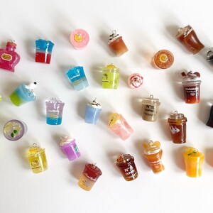 Puede incluir: Una colecci&oacute;n de dijes en miniatura con forma de bebidas de diversos colores y estilos, incluyendo tazas de caf&eacute;, vasos de refresco y bebidas frutales. Cada dije cuenta con una peque&ntilde;a argolla met&aacute;lica en la parte superior para colgar.