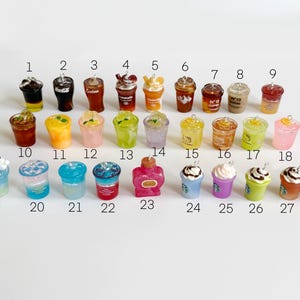 Puede incluir: Una colecci&oacute;n de veintiocho dijes de bebidas en miniatura dispuestos en tres filas, numerados del 1 al 28. Los dijes presentan varios dise&ntilde;os, incluyendo caf&eacute;s helados, bebidas con infusi&oacute;n de frutas y bebidas con crema batida.