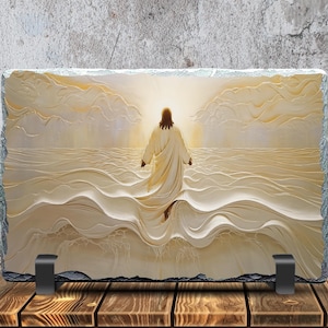 May include: A rectangular stone plaque depicting a religious scene of a figure in a white robe walking on water towards a bright light. The image is set against a textured background and supported by black metal stands. The plaque is displayed on a wooden surface.