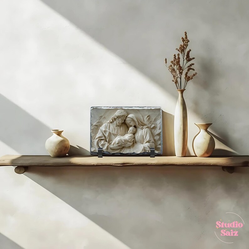 May include: A white stone relief sculpture of the Holy Family, depicting Mary, Joseph, and baby Jesus. The sculpture is mounted on a black slate base and displayed on a wooden shelf with two ceramic vases.