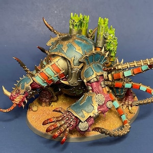 May include: A multi-colored, detailed, plastic model of a monstrous creature with multiple limbs and a large head. The creature is painted in shades of blue, red, gold, and green. The model is posed on a sandy base.