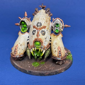 May include: A white and green detailed miniature of a sci-fi robot with a large mouth and multiple guns. The robot is standing on a brown base.