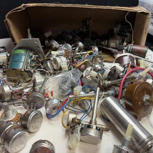 May include: A collection of assorted electronic components including various potentiometers, rotary switches, and small transformers with attached colored wires, some housed in a brown cardboard box labeled with Hitachi Cable text.