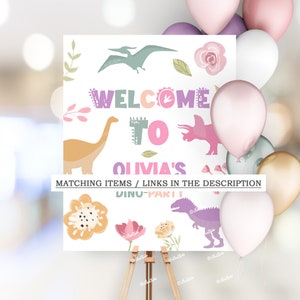 Pode incluir: Uma placa branca em um cavalete com o texto "WELCOME TO OLIVIA'S" e "DINO-PARTY" em letras coloridas. A placa apresenta ilustra&ccedil;&otilde;es de dinossauros e detalhes florais. Bal&otilde;es em rosa, roxo e dourado no fundo.