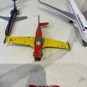 以下が含まれることがあります： 塗装が剥げた赤と黄色のプロペラ機、濃い青のジェット機、白いグローブスター旅客機、そして赤、黄、青の小さな戦闘機など、ダイキャスト製の飛行機のおもちゃのコレクションです。