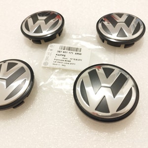 Könnte beinhalten: Vier silber-schwarze Volkswagen Radnabenabdeckungen mit dem VW-Logo. Ein weißes Etikett mit Text ist ebenfalls sichtbar. Die Kappen sind neu und scheinen in gutem Zustand zu sein.