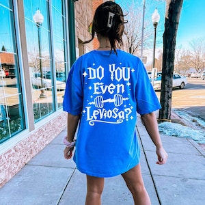 May include: A blue t-shirt with a white graphic that says "Do you even LevioSA?" with a dumbbell graphic. The shirt is being worn by a person walking down a sidewalk.