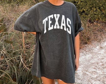 Puede incluir: Una camiseta de gran tamaño de color gris oscuro con la palabra "TEXAS" impresa en blanco en la parte delantera.