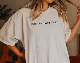 May include: A white oversized t-shirt with the text "run the dang ball" printed in black.