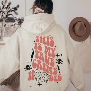 May include: A white hoodie with a pink graphic that says "This is my true crime hoodie" with a skull, knife, and smiley face design.
