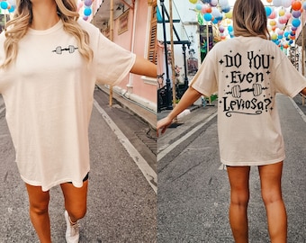 May include: A cream colored t-shirt with a black graphic on the front and back. The graphic on the front is a dumbbell. The graphic on the back says "Do you even LevioSA?" with a dumbbell graphic above the text.