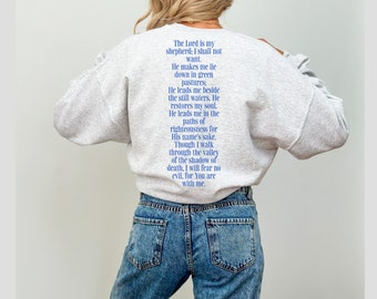Könnte beinhalten: Ein graues Sweatshirt mit einem blauen Textaufdruck auf der Rückseite. Der Text ist ein Zitat aus der Bibel, Psalm 23: "Der Herr ist mein Hirte, mir wird nichts fehlen. Er weidet mich auf grünen Auen und führt mich zum stillen Wasser. Er gibt meiner Seele neue Kraft; er führt mich auf rechten Wegen, um seines Namens willen.  Selbst wenn ich durch das finstere Tal gehe, fürchte ich kein Unheil, denn du bist bei mir.  "