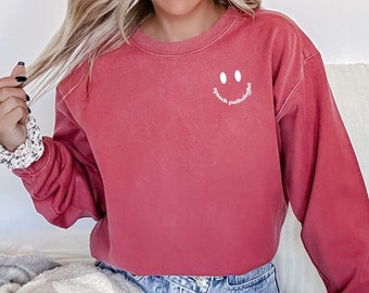 Puede incluir: Una sudadera roja con una carita sonriente blanca y el texto "speech pathologist" debajo.