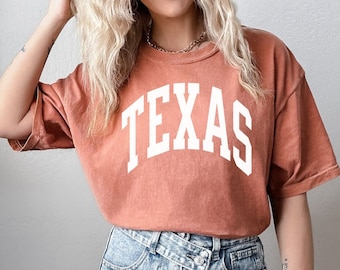 Puede incluir: Una camiseta de color óxido con la palabra "TEXAS" impresa en blanco en una fuente de estilo universitario.