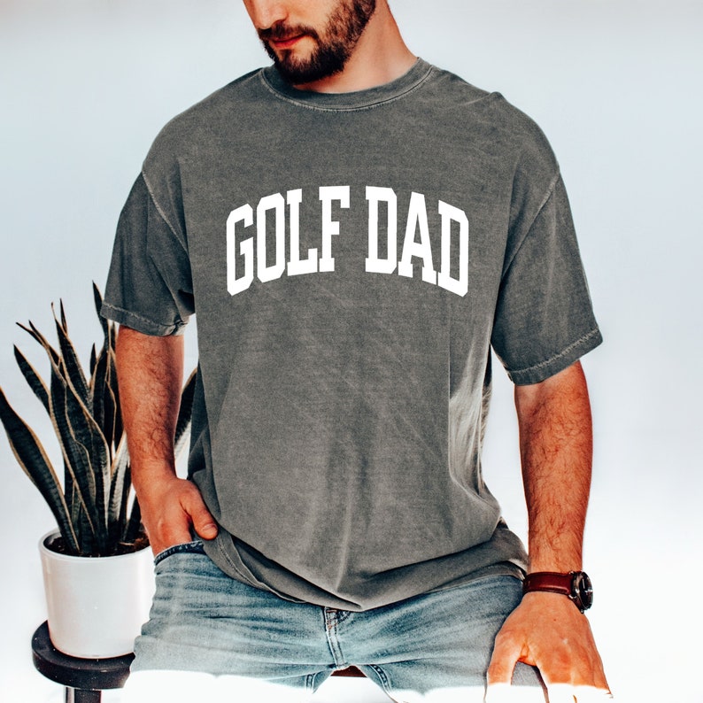 May include: A grey t-shirt with the text "GOLF DAD" in white letters.