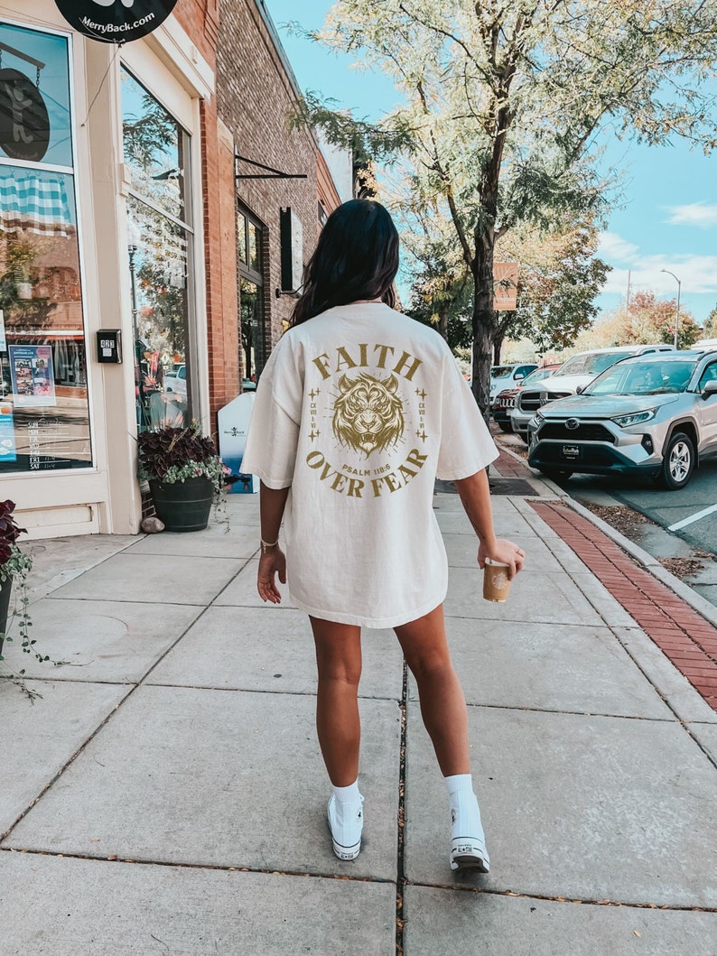 May include: A white t-shirt with a gold graphic of a tiger with the words "FAITH OVER FEAR" and "PSALM 118:6" printed on the back.