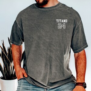 May include: A dark gray t-shirt with the text "TITANS 24" printed on the front in white.