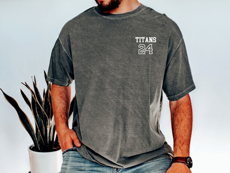 May include: A dark gray t-shirt with the text "TITANS 24" printed on the front in white.