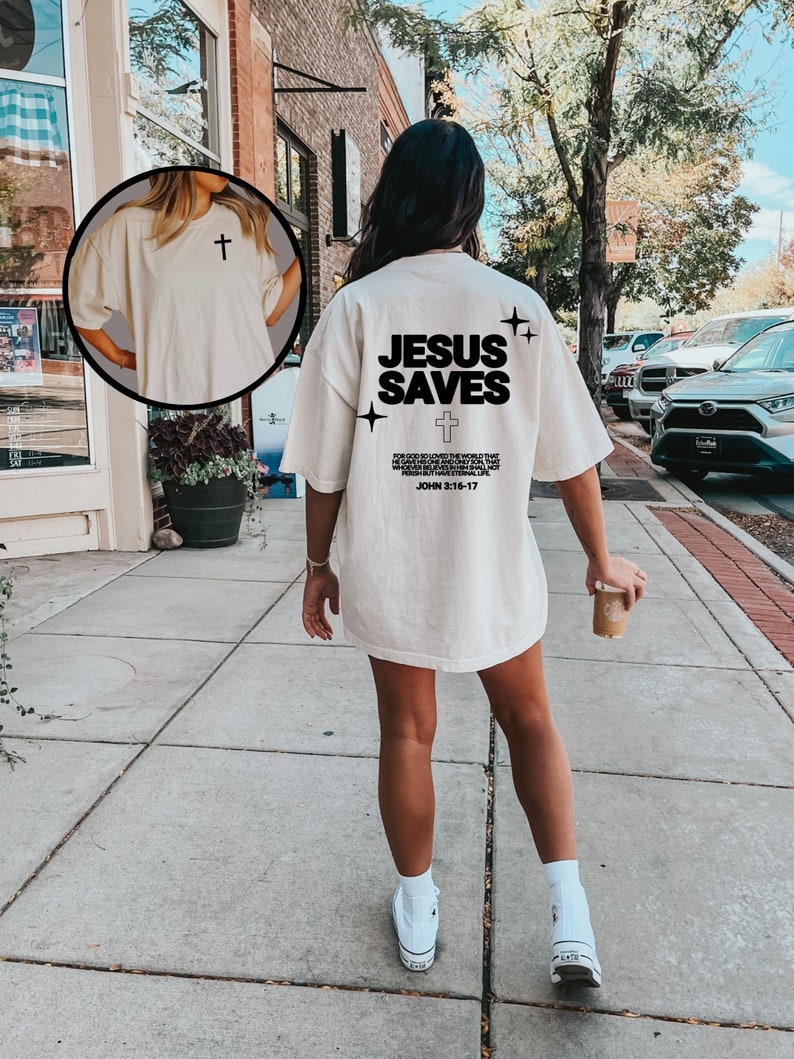 May include: A white oversized t-shirt with the text "JESUS SAVES" printed on the back. The shirt also features a small cross and the Bible verse John 3:16-17.