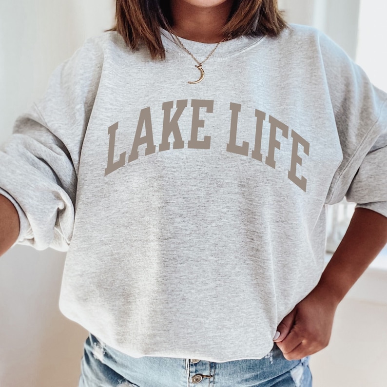 以下が含まれることがあります： グレーのトレーナーに、前面に茶色の「LAKE LIFE」の文字がプリントされています。トレーナーはゆったりとしたフィット感で、クルーネックです。