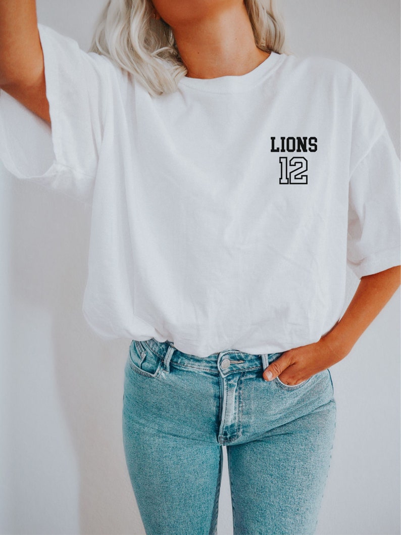 May include: White t-shirt with a black graphic that says "LIONS 12" on the left chest.