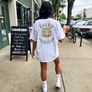 May include: White t-shirt with a gold tiger graphic and the text "FAITH OVER FEAR" and "PSALM 118" printed on the back.