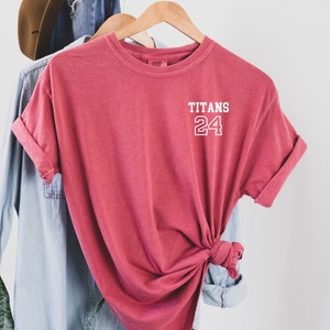 May include: A red t-shirt with the words "TITANS 24" printed on the front in white.