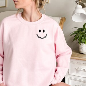 May include: A pink sweatshirt with a black smiley face and the text "social worker" on the front.