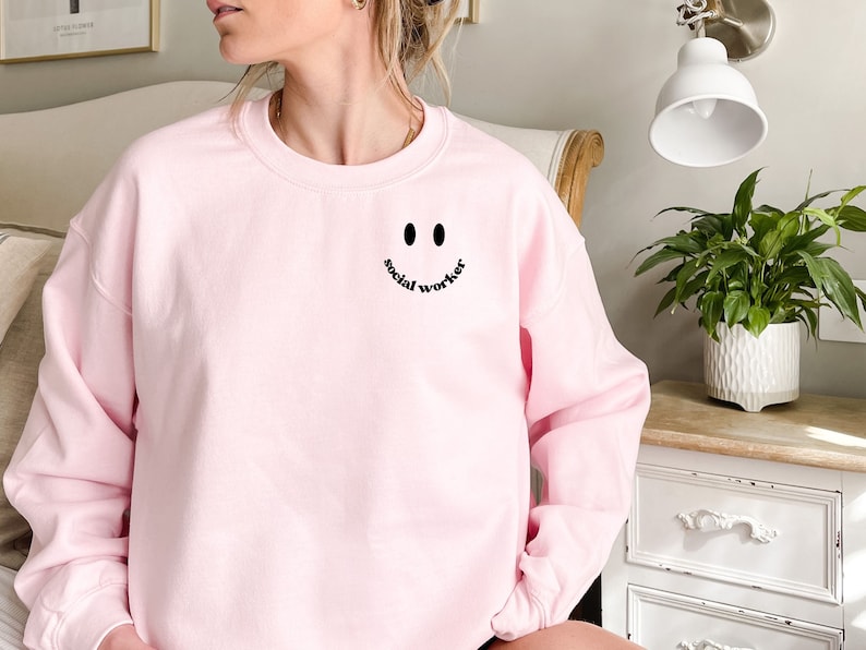 May include: A pink sweatshirt with a black smiley face and the text "social worker" on the front.