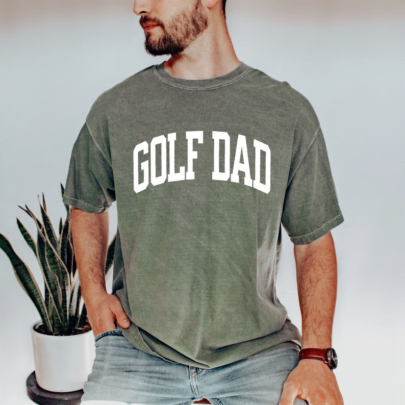 May include: A green t-shirt with the text "GOLF DAD" in white letters.