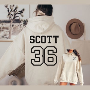 May include: A cream-colored hoodie with a black print of the name "SCOTT" and the number "36" on the back.