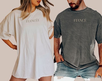 May include: Two oversized t-shirts with the words "Fiancé" and "Fiancée" printed on them. The shirts are in a distressed style and are a light gray and white.