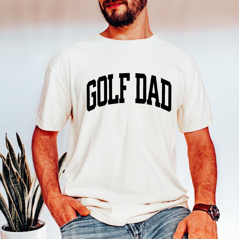 May include: A white t-shirt with the text "GOLF DAD" printed in black.