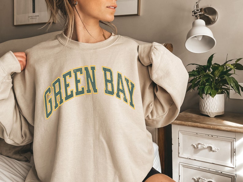 May include: A beige sweatshirt with a green and yellow arched graphic that says "GREEN BAY".