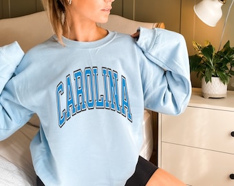 May include: A light blue sweatshirt with the word "CAROLINA" printed in a blue and gray arch across the front.