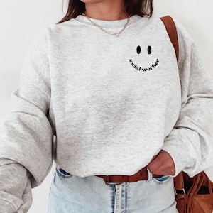 May include: A grey sweatshirt with a black smiley face and the text "social worker" underneath.