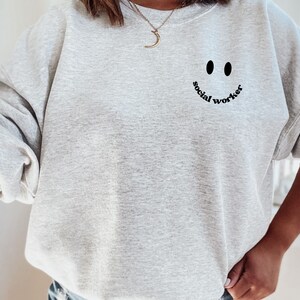 May include: Grey sweatshirt with a black smiley face and the text "social worker" underneath.