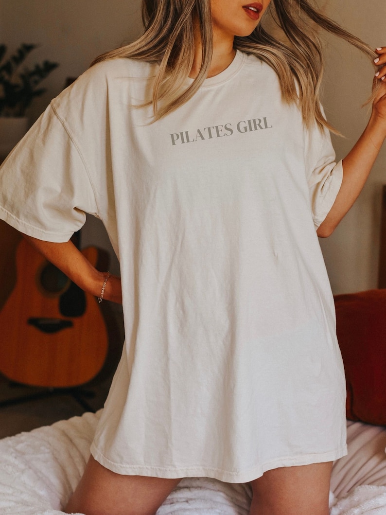 K&ouml;nnte beinhalten: Ein wei&szlig;es Oversize-T-Shirt mit dem Aufdruck "PILATES GIRL" auf der Vorderseite.