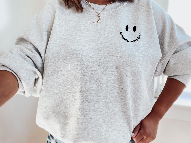May include: Gray sweatshirt with a black smiley face graphic and the text "behavior analyst" written around the smile.